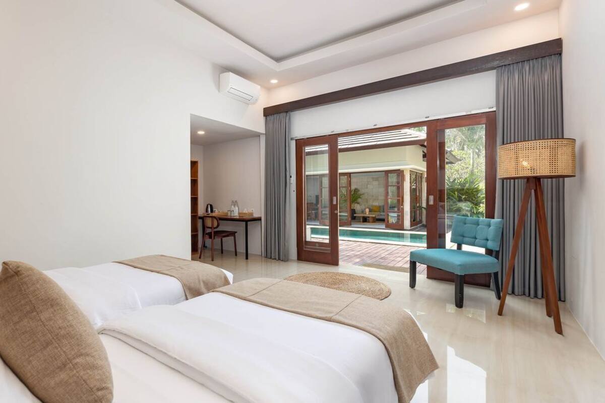 A hotel room with two beds, a desk, a chair, and a view of a pool.