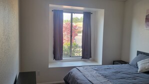 A bedroom with a bed, a window with curtains, a nightstand, and a painting on the wall.