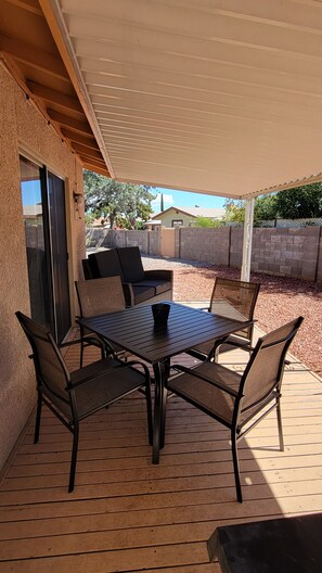 Une terrasse extérieure avec une table et des chaises, un espace abrité et une vue sur le quartier environnant.