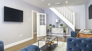 Una sala de estar moderna con una televisión de pantalla plana, una escalera y mobiliario tapizado en azul.