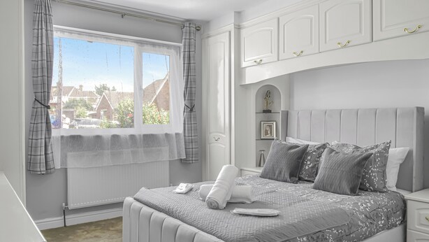 Un dormitorio con cama, mesitas de noche, una ventana con cortinas y vistas a casas.
