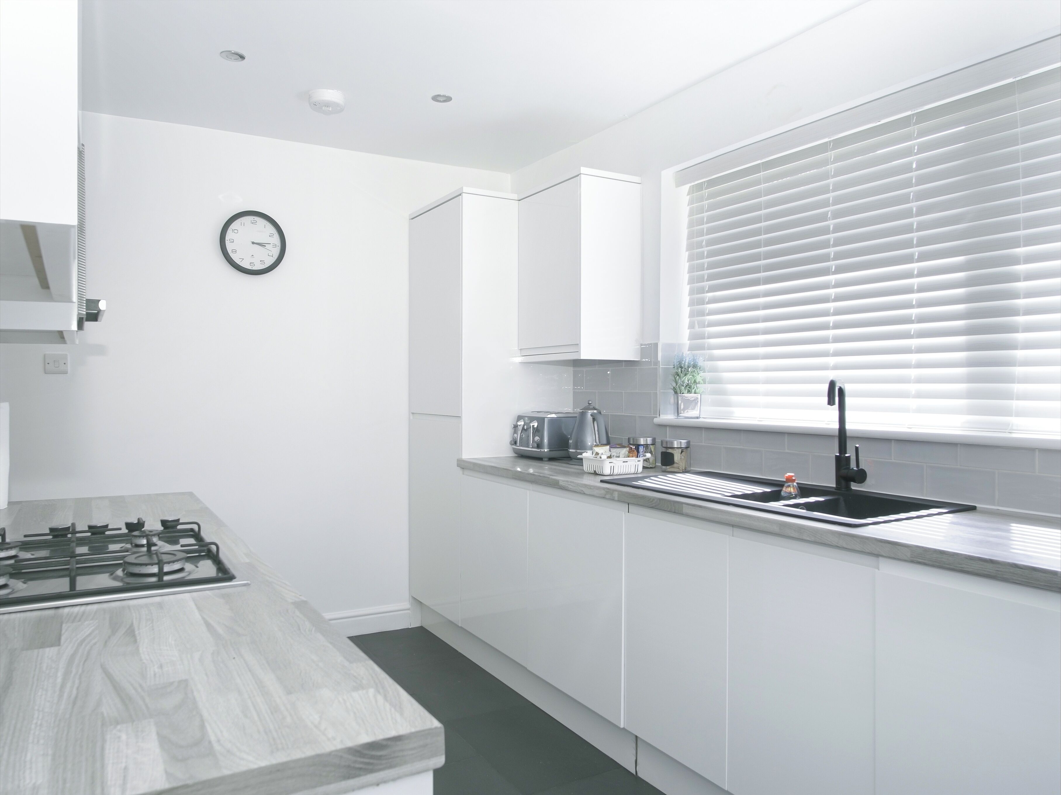A modern kitchen with white cabinetry, a gas stove, a sink, and a window with blinds.