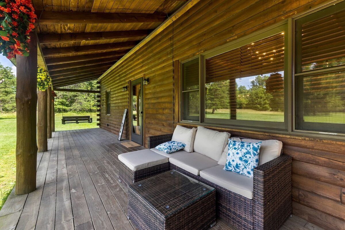 A wooden cabin with a covered porch, a wicker sofa with cushions, and a glass coffee table.