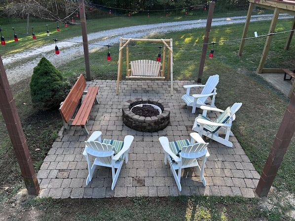 A covered outdoor seating area with a fire pit, wooden bench, and Adirondack chairs.