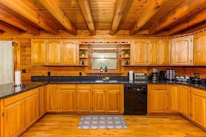 A wooden cabin-style kitchen with wooden cabinets, a granite countertop, a dishwasher, and a window above the sink.