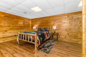 A wooden-paneled room with a bed, two bedside tables, and a ceiling light.
