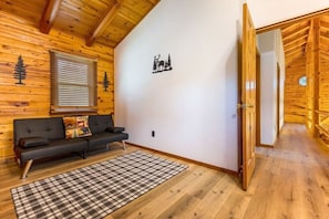 A log cabin interior with a sofa, plaid rug, and a wall with a deer and tree silhouette.