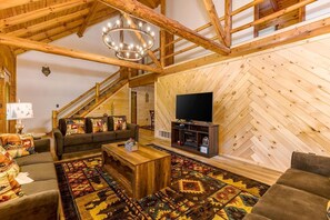 Uma sala de estar espaçosa com parede de madeira em padrão herringbone, uma televisão de tela plana grande e uma área de estar aconchegante com um sofá e uma mesa de centro.