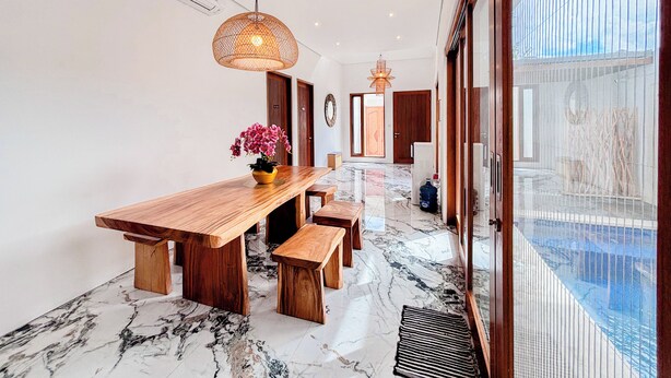 A modern dining area with a wooden table, benches, and a vase of flowers. - Budayana Villa (Jimbaran)