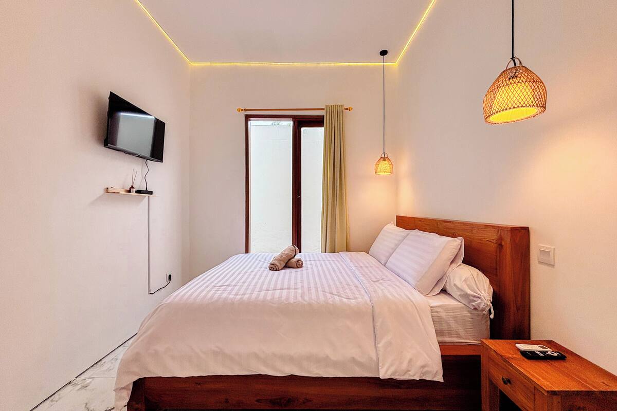 A bedroom with a wooden bed, a TV mounted on the wall, and a bedside table with a lamp.