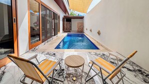A swimming pool with two lounge chairs and a table, surrounded by a white wall and a wooden ceiling. - Budayana Villa (Jimbaran)