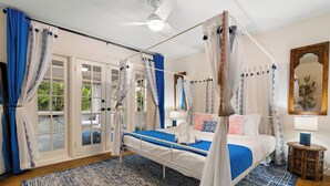 A bedroom with a four-poster bed, a ceiling fan, and a view of the outdoors through glass doors.