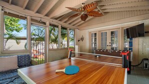 A pool table with a ceiling fan, a sofa, and a TV mounted on the wall.