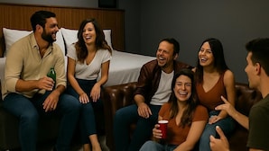 A group of people sitting on a couch in a room with a bed and a wooden headboard.