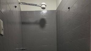 A small, dimly lit bathroom with a toilet, a shower head, and a trash bin.