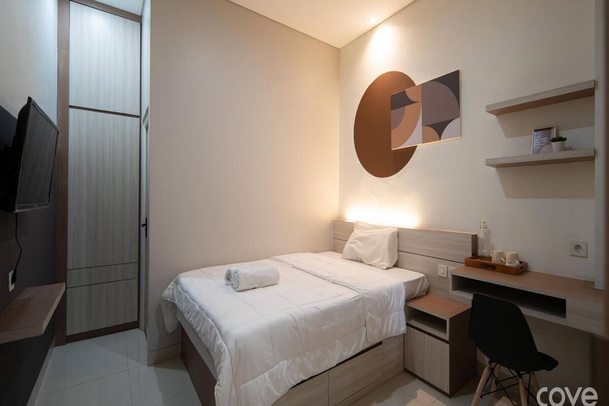 A modern bedroom with a bed, bedside table, desk, chair, and a TV.