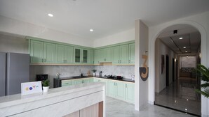 Una cocina moderna con armarios verde claro, encimera de mármol y refrigerador de acero inoxidable.