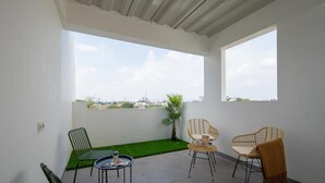 Un balcón con vista a un horizonte urbano, un pequeño jardín y tres sillas de mimbre.