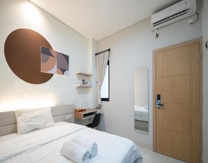 A modern hotel room with a bed, a desk, a chair, a wardrobe, and an air conditioning unit. - Cove Palacio (Jakarta)