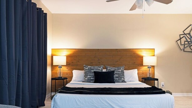 Una habitación de hotel moderna con cabecera de madera, dos lámparas de noche, una cama grande con ropa de cama blanca y un ventilador de techo.