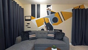 Una sala de estar moderna con un sofá seccional gris, una mesita de centro redonda y una pared decorada con arte abstracto.