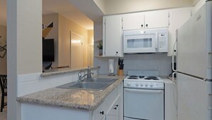 Cocina compacta con armarios blancos, encimera de granito, microondas integrado, estufa y refrigerador.
