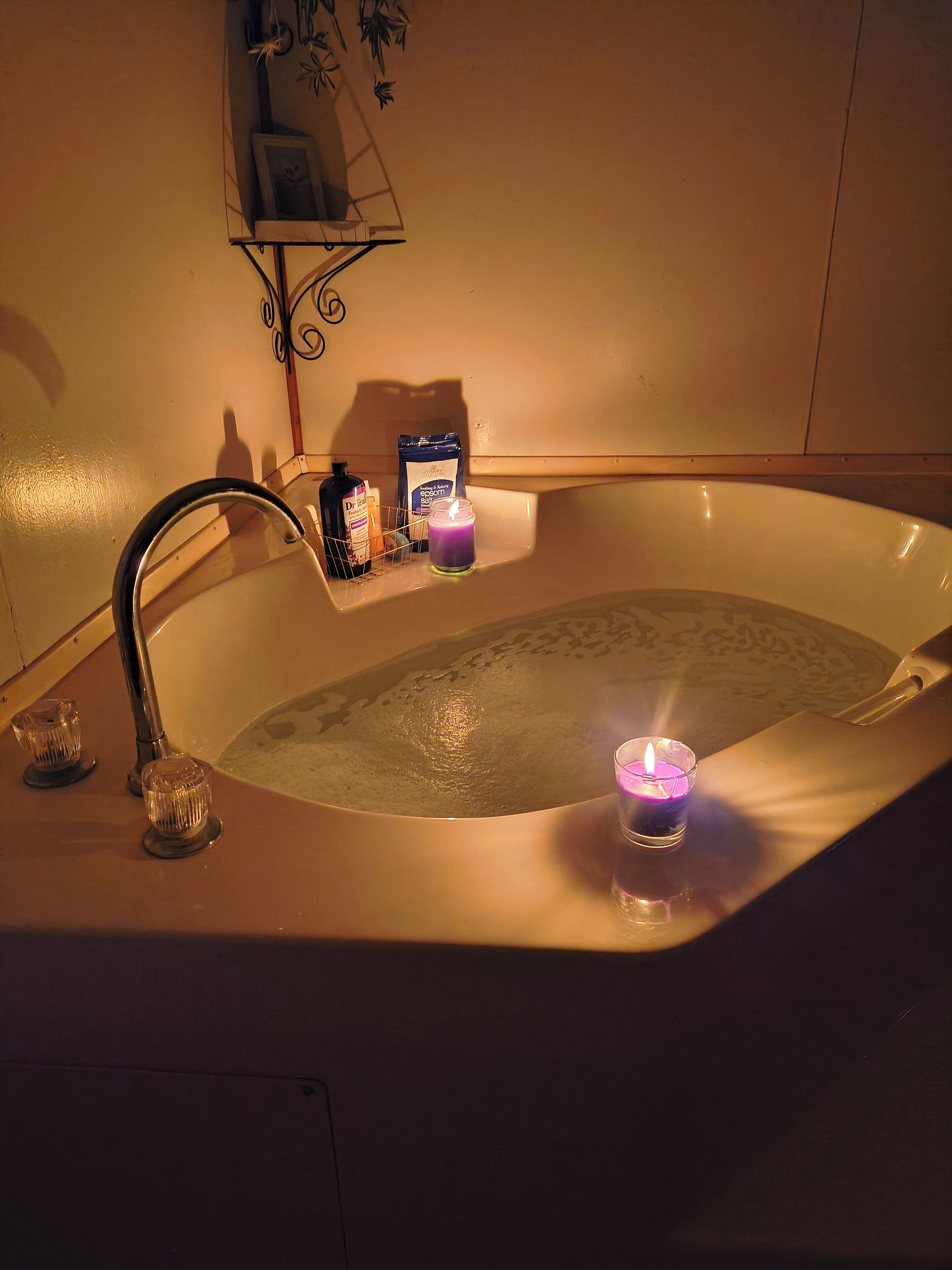 A bathtub with a running faucet, a candle, and toiletries on a shelf.