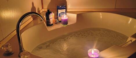 A bathtub with a running faucet, a candle, and toiletries on a shelf.