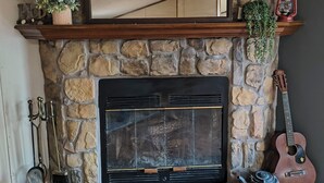 A stone fireplace with a mirror above it, a guitar, a lantern, and a small plant on the mantel.