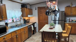 A kitchen with wooden cabinets, a stainless steel refrigerator, a dining table with chairs, and a hanging pot rack.