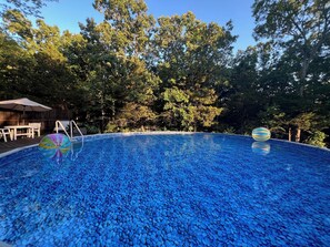 Una piscina con diseño de mosaico azul, rodeada de árboles y un deck de madera con mobiliario exterior.