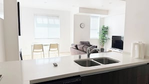 A modern kitchen with a dishwasher, a sink, and a dining area with chairs and a sofa.