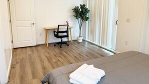 A bedroom with a bed, a desk, and a potted plant.
