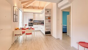 A modern kitchen with white cabinets, a dining area with a table and chairs, and a hallway leading to a bedroom.