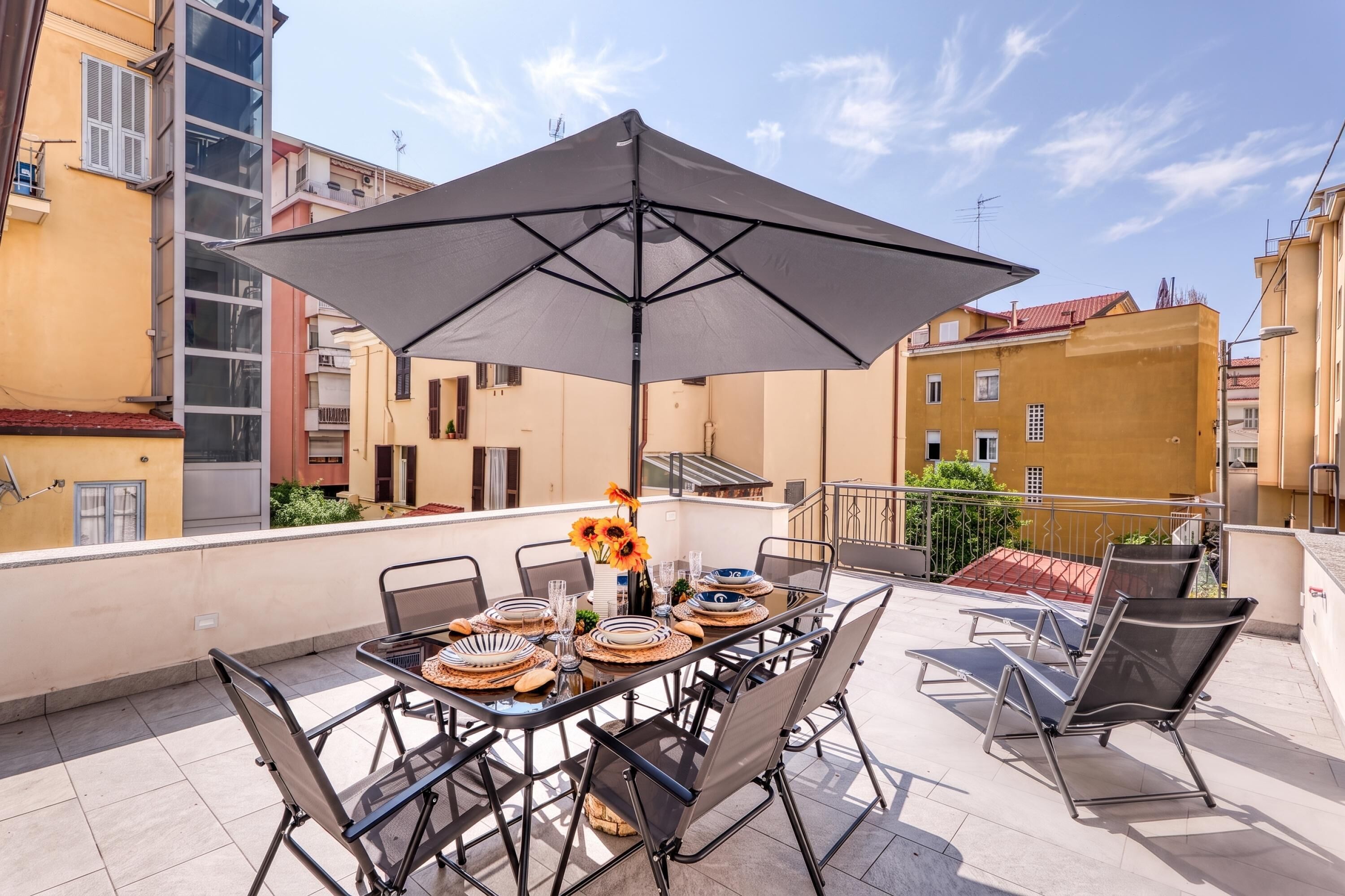 An outdoor dining area with a table set for four, surrounded by chairs, under a large umbrella.