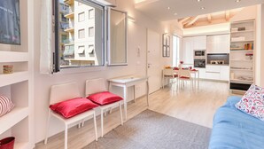 A modern apartment with a dining area, kitchen, and a living room with a sofa and chairs.