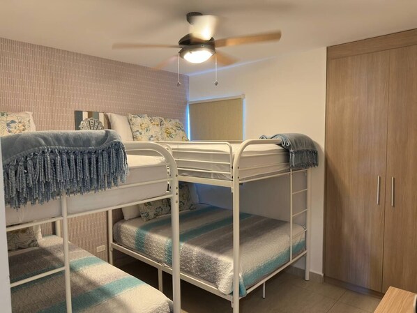 A bunk bed room with a ceiling fan, a wardrobe, and a window.
