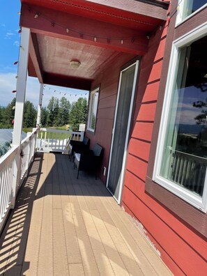 A covered outdoor area with a table and chairs, a railing, and a view of the surrounding landscape.