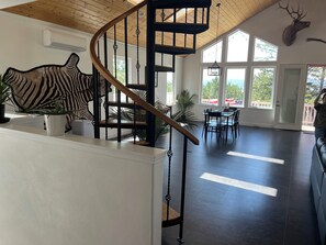 Amplia habitación con una escalera de madera, un adorno en la pared con estampado de cebra y un ventanal con vistas.