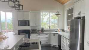 Uma cozinha moderna com armários brancos, geladeira de aço inoxidável, micro-ondas embutido e uma ilha grande com fogão.