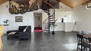 Ein großzügiger Wohnbereich mit einem schwarzen Ledersofa, einer Holztreppe und einem aufgehängten Hirschkopf.