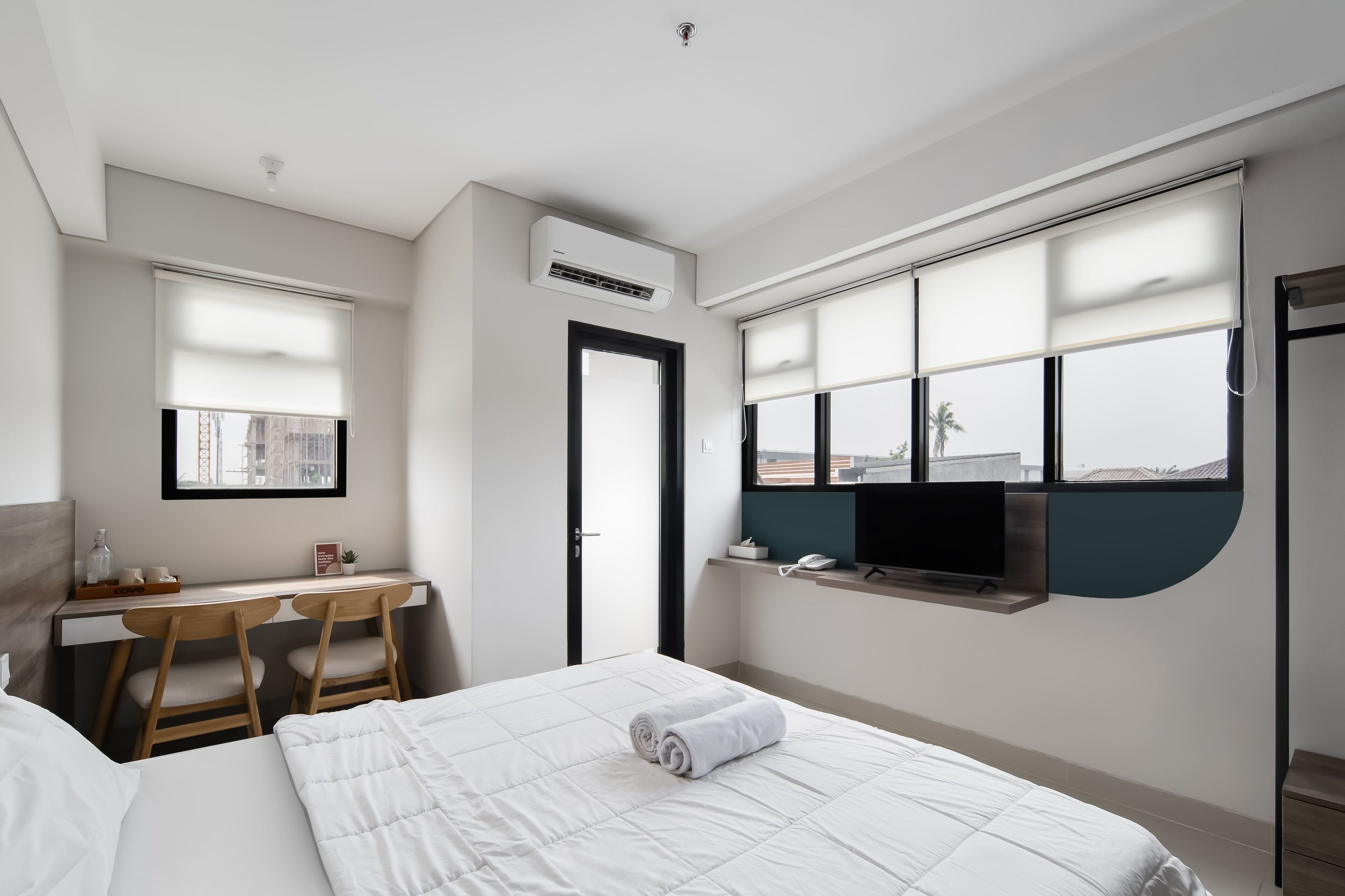 A hotel room with a bed, a desk, two chairs, a TV, and a window with a view.