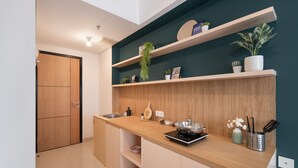 A modern kitchen with wooden cabinets, a wooden countertop, and built-in shelves with plants and kitchenware. - Cove Aspena Residence (Tangerang)
