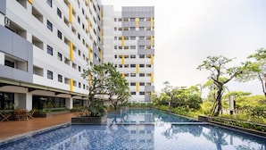 A modern hotel with a pool area, outdoor seating, and lush greenery. - Cove Aspena Residence (Tangerang)