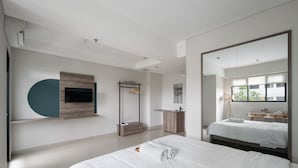 A modern bedroom with a large bed, a TV mounted on the wall, a wooden vanity, and a large mirror. - Cove Aspena Residence (Tangerang)