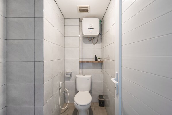 A modern bathroom with a toilet, a shower, and a built-in heater. - Cove Aspena Residence (Tangerang)