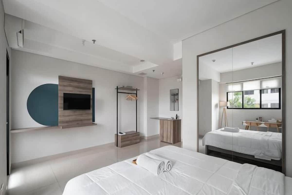Ein modernes Hotelzimmer mit einem großen Bett, einem an der Wand montierten Fernseher, einem Kleiderschrank und einem Schreibtisch mit Stuhl.