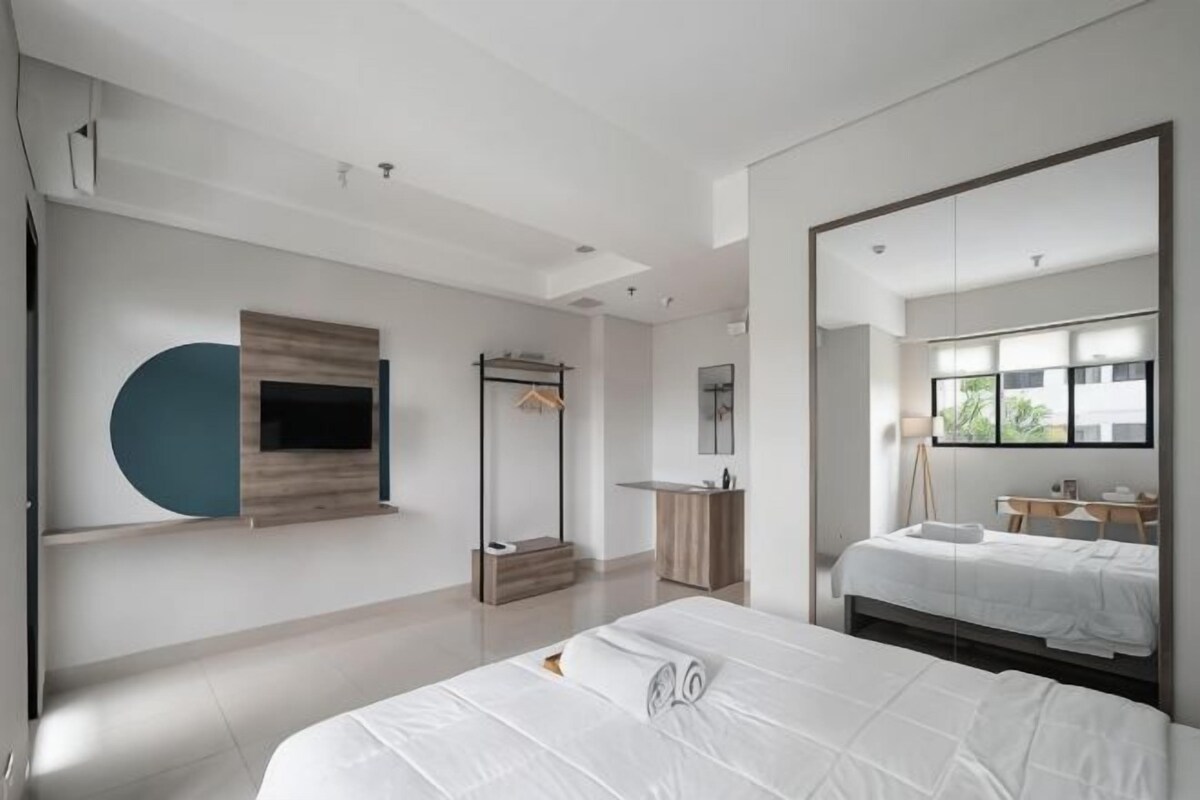A modern hotel room with a large bed, a TV mounted on the wall, a wardrobe, and a desk with a chair.