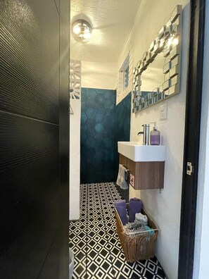 A bathroom with a geometric patterned floor, a mirrored wall, and a wooden vanity with a towel rack. - NUEVA VISTA INN (La Cruz de Huanacaxtle)