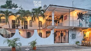 Un hotel con fachada blanca, varios balcones y palmeras.